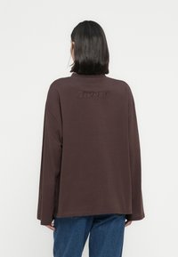 Καφέ μπλούζα μακρυμάνικη με άνετη εφαρμογή, με ψηλό λαιμό και κεντημένο το "2ND DAY" στο πίσω μέρος. Απαλό ύφασμα με ελάχιστη υφή.