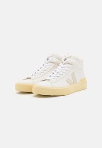 High-top sneakers in white leather with beige accents, textured rubber sole, and white laces. Features a logo detail on the side.