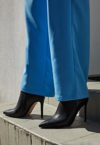 Stivali alti neri con tacco a spillo e punta appuntita, con una texture scintillante. Abbinati a pantaloni blu larghi che arrivano fino alle caviglie.