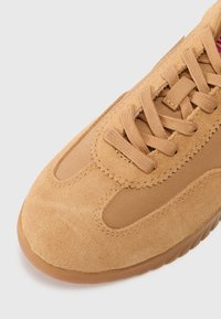 Zapatillas de ante color marrón con panel de malla, cordones planos, detalles cosidos y suela de goma con un acabado texturizado.