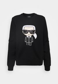 Černá mikina s potiskem postavičky v kresleném stylu, s bílými vlasy, slunečními brýlemi a designem obleku na přední straně, vyrobená ze směsi bavlny.