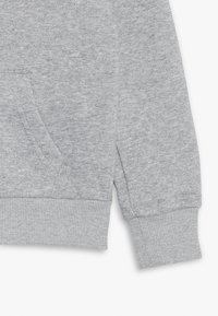 Sweatshirt gris avec une finition texturée, présentant une poche avant, des poignets et un ourlet côtelés. Tissu doux avec un design décontracté.