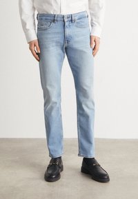 Jean en denim bleu clair avec une coupe droite, présentant un design classique à cinq poches et un léger effet délavé. Associé à des mocassins noirs.