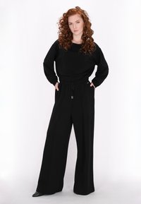 Zwarte oversized sweatshirt met een brede halslijn en lange mouwen, gecombineerd met hoge zwarte wijde broek. Touwtjes in de taille.