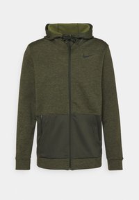 Sweat à capuche zippé vert olive avec un tissu texturé, capuche à cordon de serrage et logo Nike noir sur la poitrine. Comprend des poches latérales zippées.