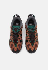 Bruna och gröna sportskor med överdel i nät och läder, med svarta skosnören, texturerade sulor och logotypdetaljer.