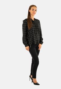 Blusa de cuadros en blanco y negro con cierre de botones, combinada con pantalones negros ajustados y zapatos de tacón alto negros. Acabado de tela suave.