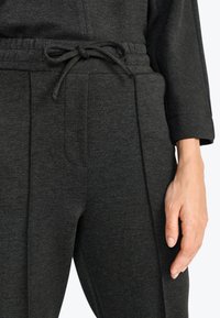 Donkergrijze jogpants van zachte stof. Voorzien van een elastische tailleband met verstelbare trekkoorden en zijzakken. Gladde textuur.