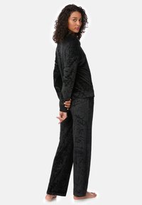 Conjunto de pijama de felpa negra que incluye un top de manga larga y pantalones con un patrón abstracto texturizado. Material suave para mayor comodidad.