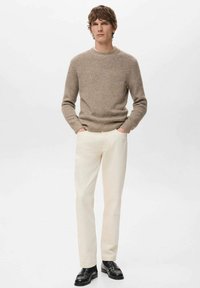 Maglione lavorato a maglia beige con motivo a zigzag, pantaloni dritti color crema e scarpe nere. Design semplice con scollo rotondo e tessuto strutturato.