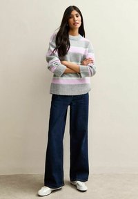 Suéter gris a rayas con líneas en rosa claro y verde. Combinado con jeans de pierna ancha en azul oscuro y zapatillas blancas. Textura de hilo suave.