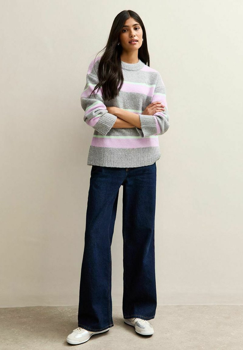 Suéter gris a rayas con líneas en rosa claro y verde. Combinado con jeans de pierna ancha en azul oscuro y zapatillas blancas. Textura de hilo suave.
