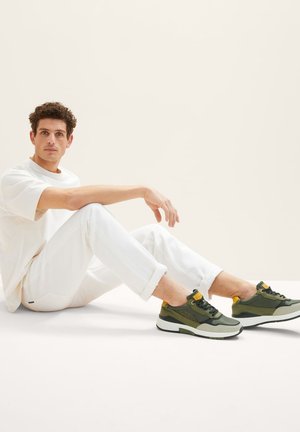 Des baskets multicolores avec un mélange de vert olive, de gris et d'accents jaunes, associées à un t-shirt blanc décontracté et à un jean blanc.