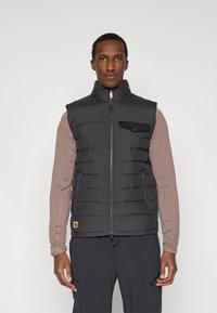 Zwarte pufferbodywarmer met een hoge kraag, een ritssluiting aan de voorkant en een borstzak. Gemaakt van doorgestikt materiaal en voorzien van een logolabel onderaan links.