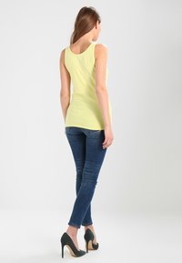 Yellow sleeveless top paired with dark blue skinny jeans and green high heels. Focus on fitted design and smooth texture of the fabric.