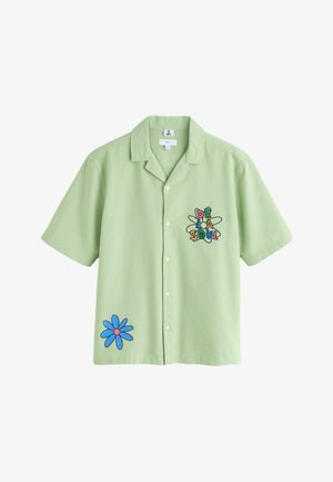 Chemise à manches courtes vert clair avec des boutons, ornée du texte coloré "De La Soul" et d'un motif d'atome sur la poitrine gauche, ainsi qu'un graphique de fleur bleue sur le bas devant.