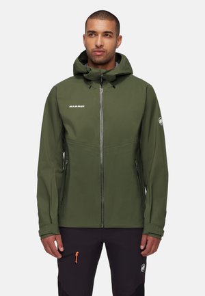 Uomo che indossa una giacca con cappuccio verde oliva con cerniera frontale e pantaloni neri con tirazip arancione su sfondo bianco.