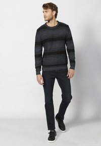 Temno siva jopica z črnimi vodoravnimi črtami, kroja s prostim vratnim izrezom, z rebrastimi manšetami, v kombinaciji z temno jeans hlačami in črnimi supergami.