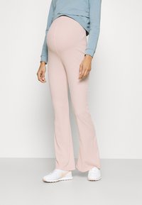 Calças flare cor-de-rosa com textura canelada, feitas de um tecido elástico, combinadas com uma blusa de manga longa azul clara e ténis brancos com detalhes subtis.