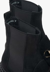 Černé kotníkové boots s kombinací semišového a elastického materiálu. Mezi pozoruhodné detaily patří zlatý kovový doplněk a strukturovaná podešev.