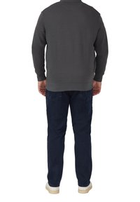 Felpa grigia scura con colletto alto, tessuto texturizzato e polsini a coste, abbinata a jeans blu scuro e scarpe di colore chiaro.