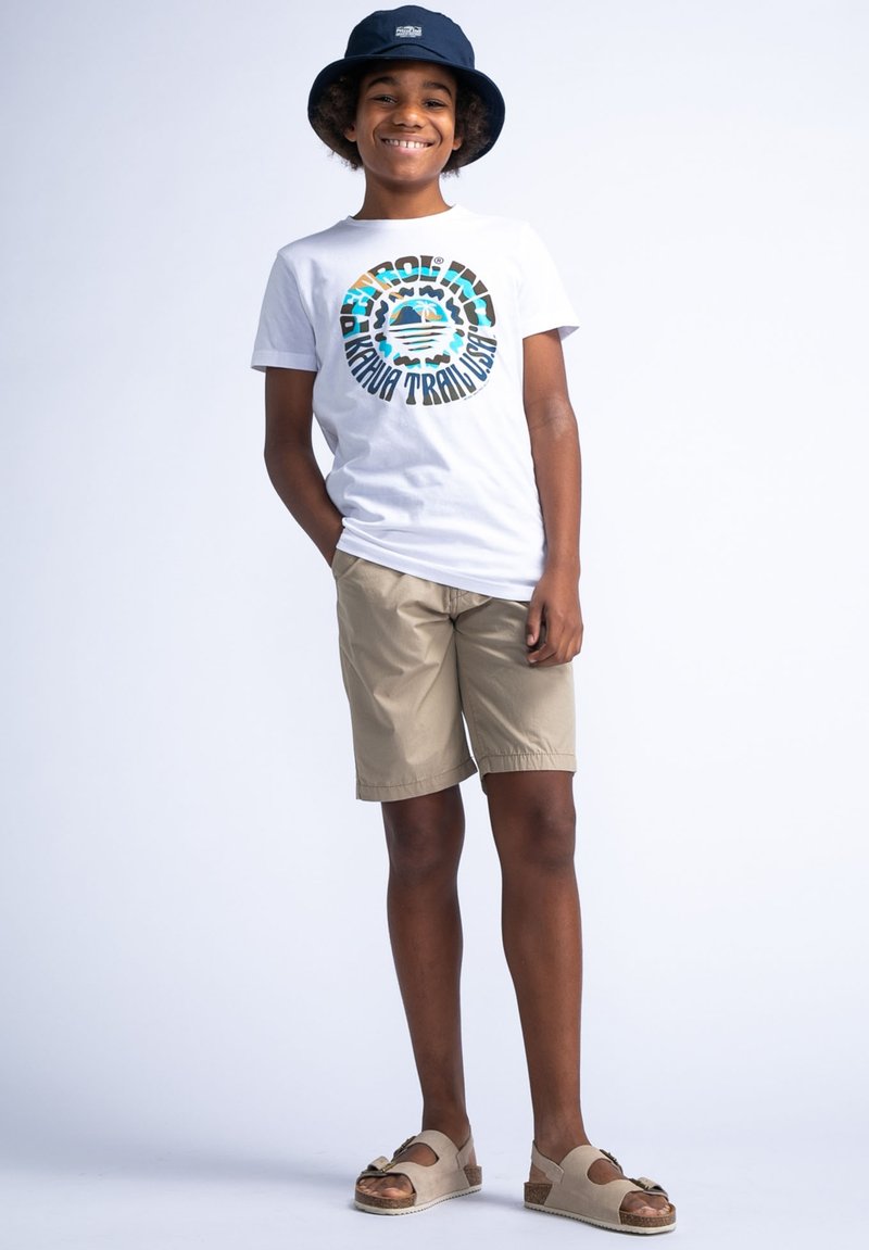Camiseta blanca con gráfico circular colorido, pantalones cortos caqui y sandalias beige. Los accesorios incluyen un sombrero de cubo azul marino. Atuendo casual.