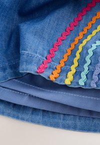 Tessuto di denim con strisce ondulate ricamate colorate in rosa, arancione, giallo, azzurro e viola lungo gli orli cuciti.