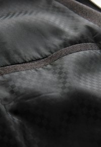 Black fabric interior with a subtle checkered pattern. Features a pocket with a dark textured trim along the opening.
