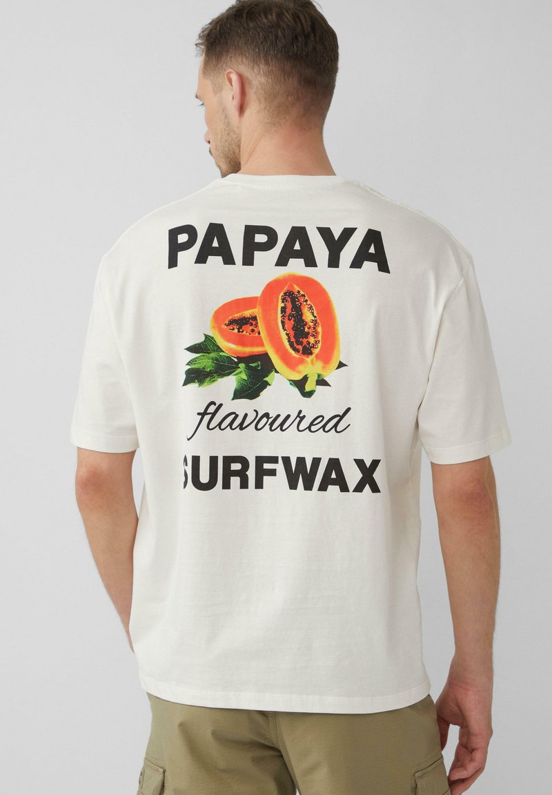 Witte katoenen t-shirt met een grafisch ontwerp van twee gehalveerde papa's en de tekst "PAPAYA smaak SURFWAX" in dikke zwarte letters.