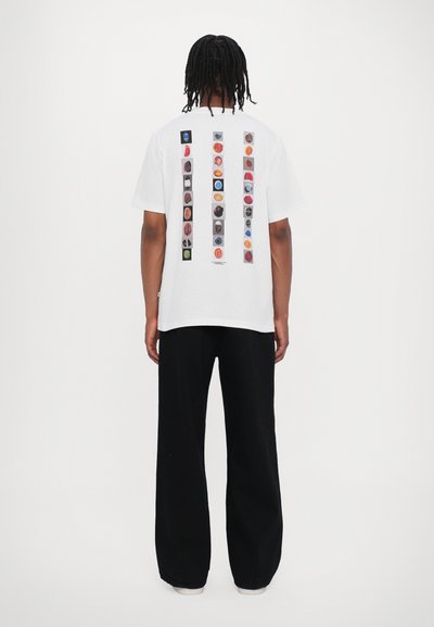 T-shirt blanc à manches courtes avec un design graphique coloré et divers icônes au dos. Associé à un pantalon large noir.