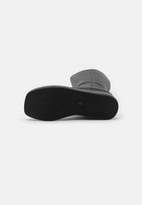 Bota de cuero negro hasta la rodilla que muestra una suela de goma texturizada con ranuras horizontales, enfatizando durabilidad y tracción.