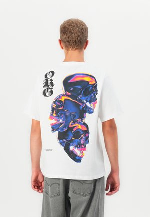 Person with short curly hair wearing a white t-shirt with neon blue and pink triple skull graphic and black gothic letters "ORG" on back.