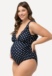 Costume da bagno premaman a pezzi unici blu navy con pois, con rifiniture a ruffle sulle spalle e un profondo scollo a V, realizzato in tessuto elastico per il massimo comfort.