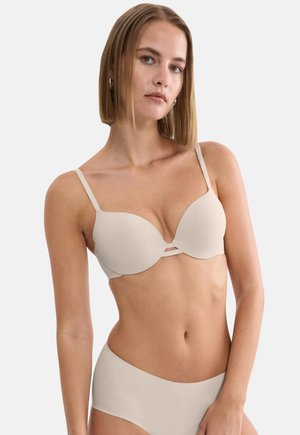 Γυναίκα με ίσια ξανθά μαλλιά, που φοράει μπεζ στηθόδεσμο με εσωτερική επένδυση και ασορτί άνετο εσώρουχο, σε απλό φόντο.