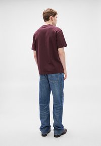 Bordo bomba majica s kratkimi rokavi, sproščenega kroja in okroglim izrezom, kombinirana z visokim pasom, širokimi modrimi kavbojkami iz jeansa.