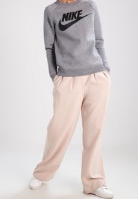 Šedá fleecová mikina s černým logem Nike, doplněná o světlé béžové kalhoty s širokými nohavicemi a bílé tenisky. Neformální outfit vhodný na volný čas.