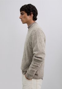 Lichtgrijze, getextureerde gebreide trui met een ronde hals. Draagt over een geruit overhemd, met opvallende geribde boorden en zoom.