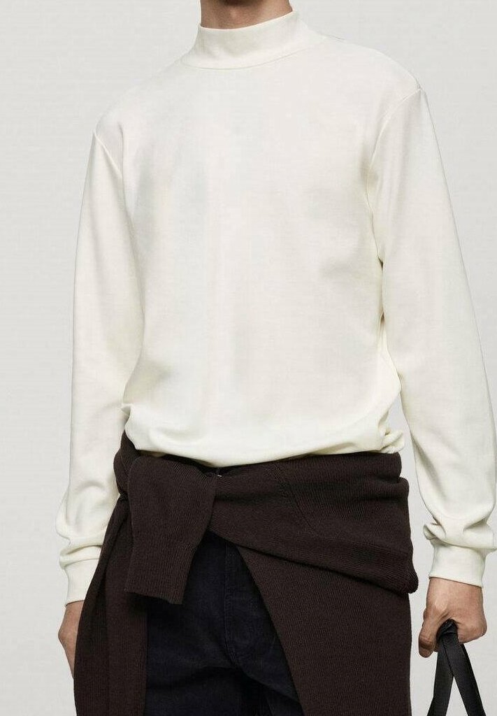 Homme portant une chemise blanche à col montant à manches longues avec un pull sombre noué autour de la taille, tenant un sac à bandoulière noir dans la main droite.