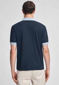 Marinblå kortärmad pikétröja med ljusblå krage och manschetter, med en ensartad textur och en avslappnad passform. Bakvy visad.