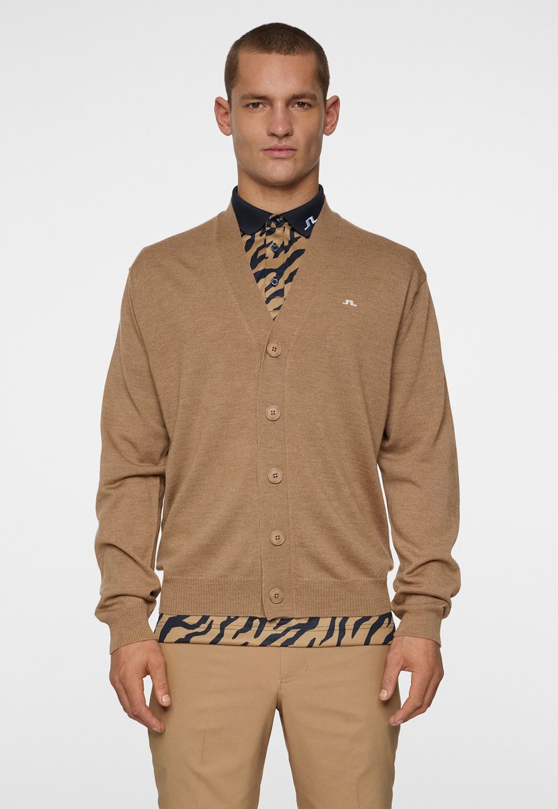 Brun cardigan med V-ringning, knappstängning och ribbade ärmslut. Bärs över en mönstrad skjorta med tigerstripor i beige och svart.