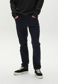 Dunkelblaue Chinos mit schlanker Passform, kombiniert mit schwarzen Wildledersneakern mit weißen Gummisohlen und cremefarbenen Schnürsenkeln. Strukturiertes Strickpullover.