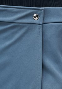 Μπλε ύφασμα με ασημένιο κουμπί στερέωσης στη μέση, φορεμένο με μαύρο ριμπ τοπ που φαίνεται από πάνω.