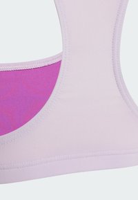 Jasnofioletowy sportowy biustonosz z gładką fakturą, zaokrąglonym dekoltem i kontrastowym różowym wnętrzem. Minimalistyczny design z czystymi szwami.