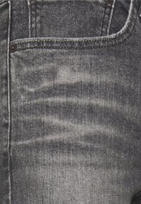 Vaqueros de mezclilla gris con un patrón ligeramente descolorido, diseño de cinco bolsillos, herrajes negros y detalle de costuras visibles a lo largo de las costuras.