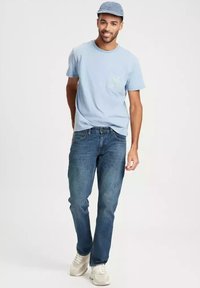 Jasnoniebieska bawełniana koszulka z kieszonką, niebieskie dżinsy i białe trampki. Strój uzupełnia dopasowana jasnoniebieska czapka.