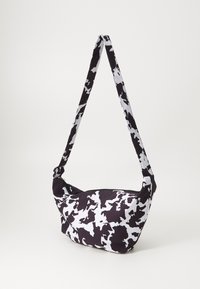 Borsa a righe bianco e nero con una forma morbida e curvilinea e una lunga tracolla regolabile. Realizzata in tessuto con chiusura a zip.