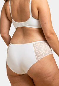 Ensemble de lingerie blanche comprenant un soutien-gorge lisse et extensible ainsi qu'une culotte taille haute avec un panneau en dentelle texturée. Les bords festonnés viennent embellir le design.