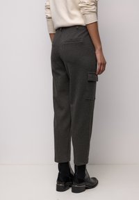 Lässig geschnittene Cargohose aus dunkelgrauem Stoff mit dezentem Muster, Seitentaschen und taillierter Knöchellänge, kombiniert mit schwarzen Stiefeln.