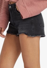 Pantalones cortos de mezclilla negra con dobladillo deshilachado, que cuentan con un diseño de cinco bolsillos y detalles desgastados. Combinados con un suéter texturizado rosa.