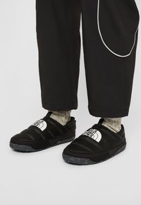 Mustat puffatut liukuvaatteet, joissa on pilkullinen harmaa pohja ja valkoinen logo. Rakennepinta, jossa on ristivöitä ja vetokahva helppoa pukemista varten.